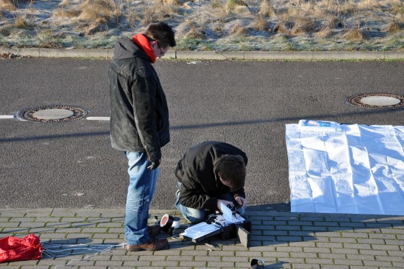 Zwei Personen bereiten am Straßenrand in Schönebeck die Sonde vor, daneben liegt der Fallschirm
